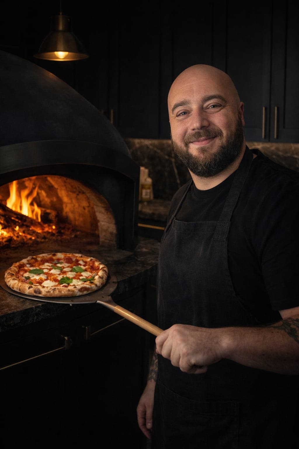 Callum, founder of Calàbbria, holding a fresh Margherita pizza on a peel in front of the lit wood-fired oven