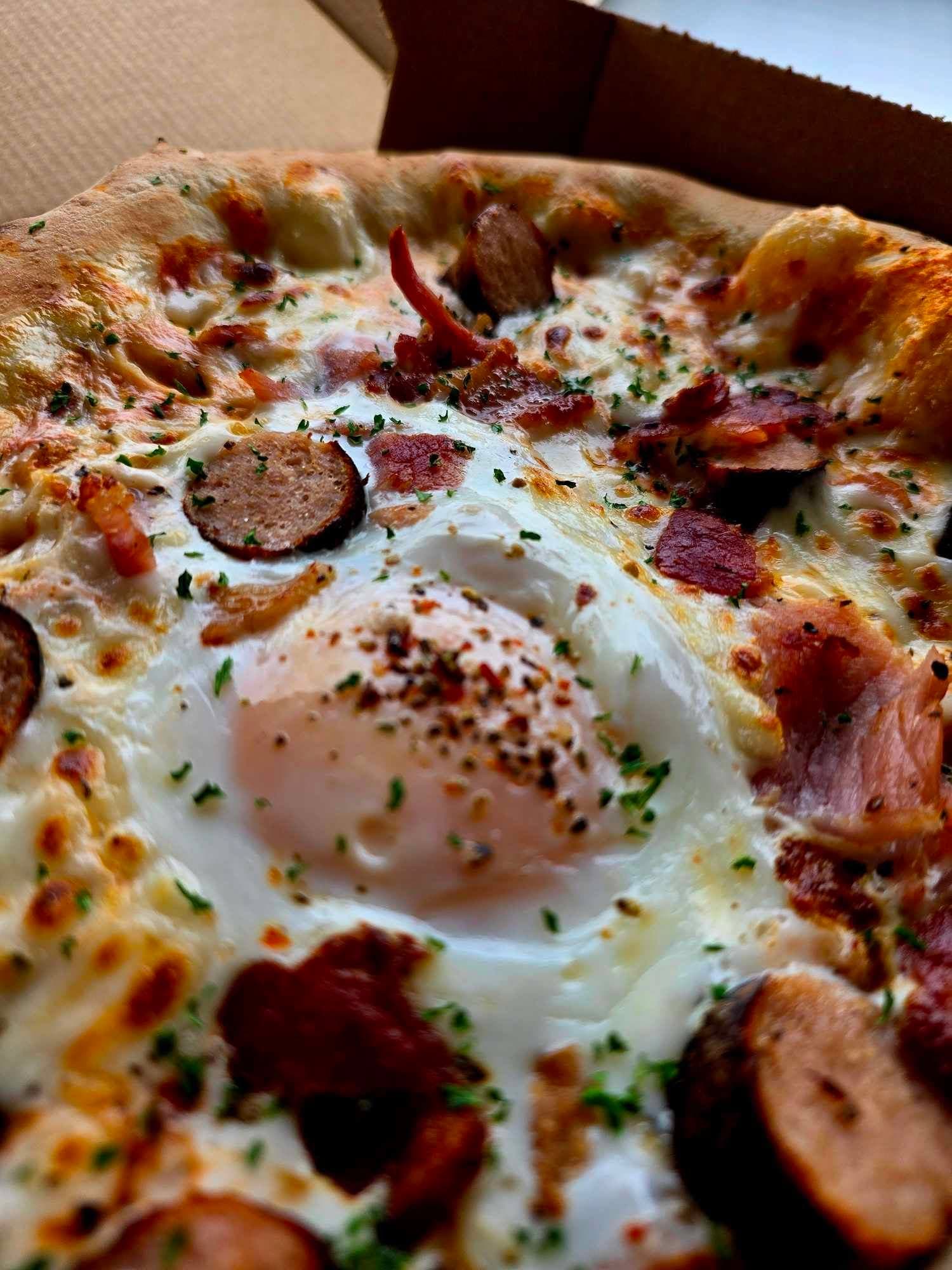Close-up of stonebaked pizza topped with a soft baked egg and pancetta