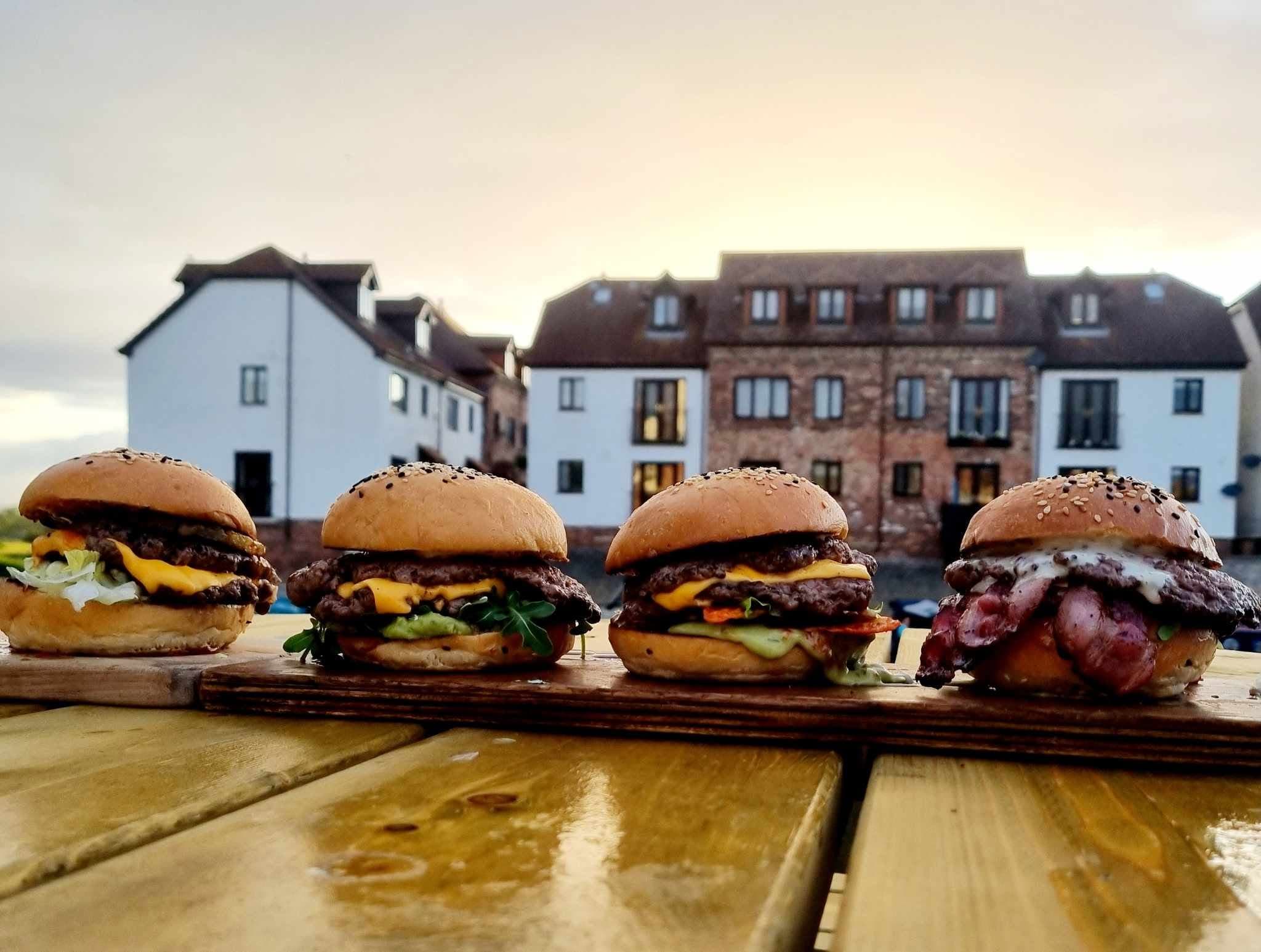 Four loaded smash burgers lined up outdoors at dusk
